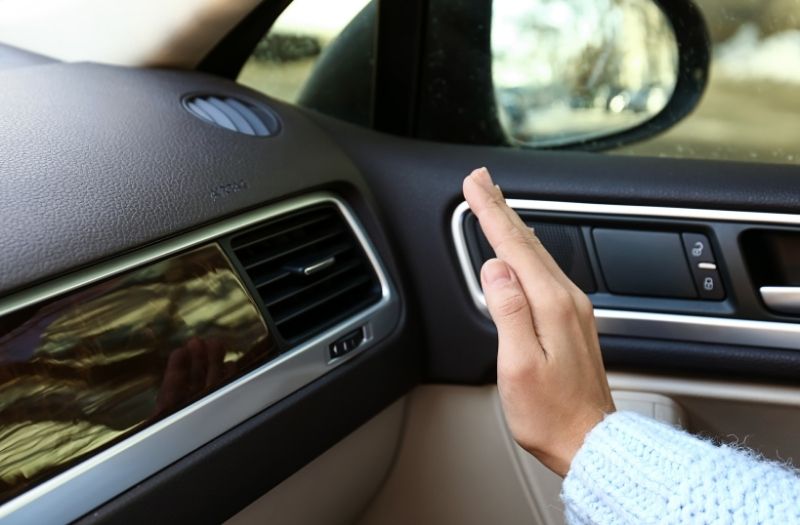 Woman checking operation of air conditioner in her car.